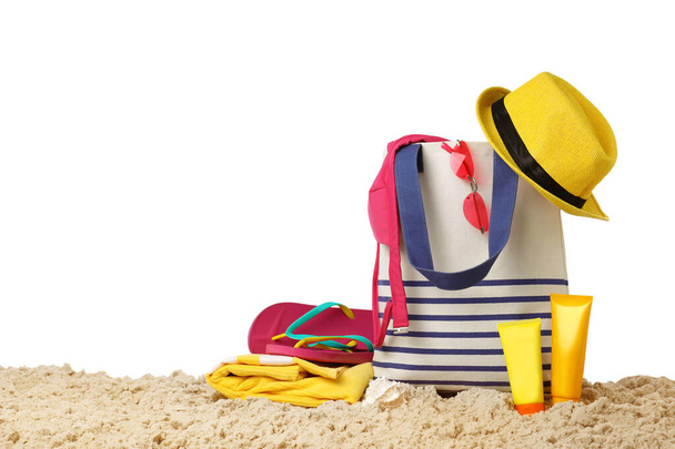 Stylish bag with beach accessories on sand against white background - 写真・画像