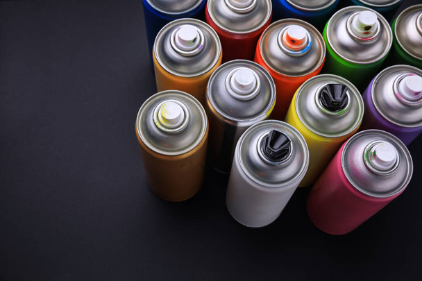 Cans of different graffiti spray paints on black background, above view - Фото, изображение