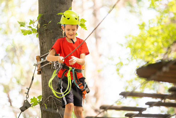 Скалолазание по высокогорному канатному парку - маленький мальчик в горном шлеме и технике безопасности - Фото, изображение