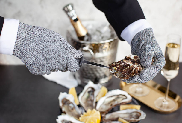 Hands of waiter in special gloves opening an oyster - Foto, imagen