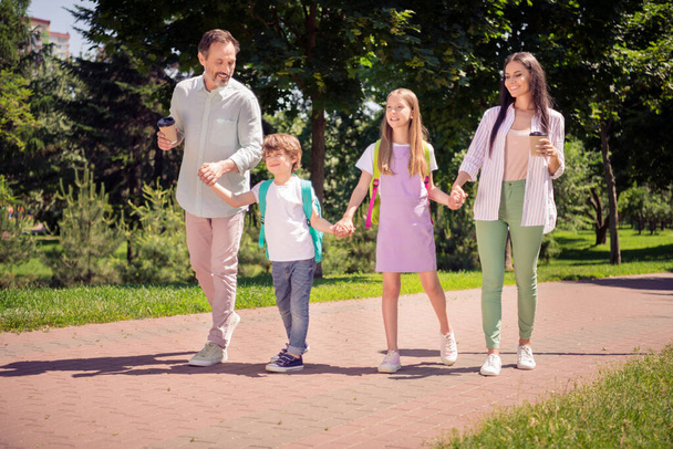 Photo of pretty sweet preteen boy girl mother father dressed casual outfit holding arms walking holding beverages outside city park - Foto, Imagem