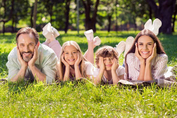 Photo of cheerful positive father mother school girl boy wear casual clothes lying green grass smiling outdoors countryside forest - Fotografie, Obrázek
