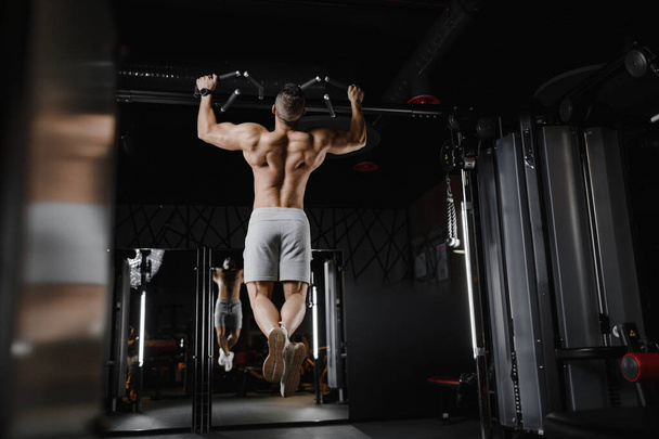 Fitness man pumping up muscle doing pull-ups exercises in gym naked torso. Handsome strong athletic men pumping up back muscles workout fitness and bodybuilding concept background - Photo, Image