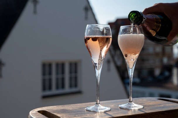 Pouring of rose champagne sparkling wine in flute glasses on outdoor terrace in France in sunny day - Photo, Image