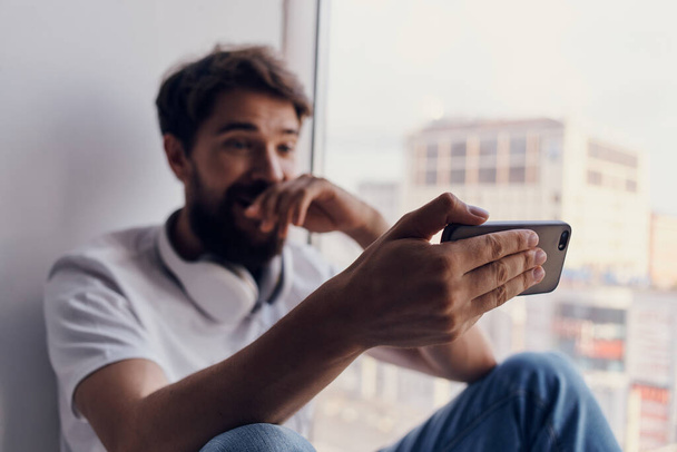 Mies istuu ikkunalaudalla älypuhelimen kanssa  - Valokuva, kuva
