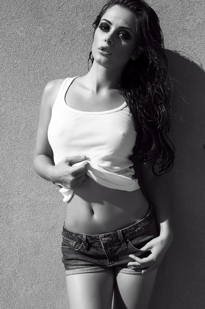 sexy girl with dark hair in jeans shorts posing beside a wall - Fotografie, Obrázek
