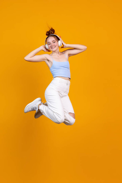 Vertical image of young cute girl jumping isolated on yellow studio background. Female fashion model in casual clothes. Concept of human emotions, natural beauty, youth - Fotografie, Obrázek