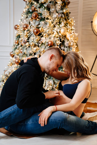 happy man and pregnant woman sitting on the floor by the Christmas tree.  - Valokuva, kuva