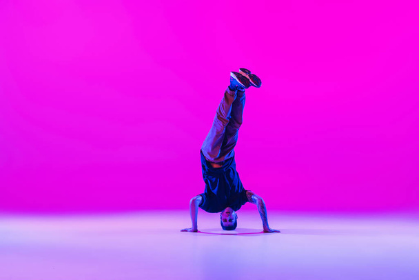 Portrait d'homme dansant, danseur de rupture en action, mouvement dans des vêtements modernes isolé sur fond de magenta lumineux à la salle de danse dans la lumière néon. - Photo, image