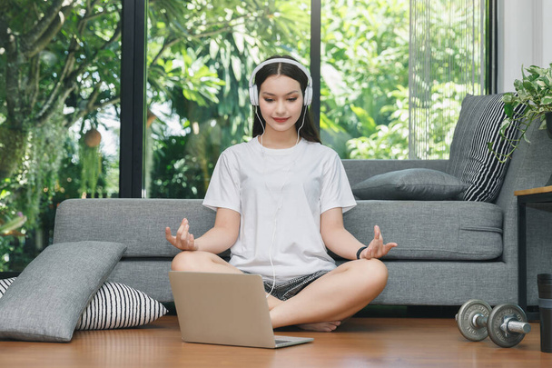 Bella giovane donna pratica tutorial di yoga online sul computer portatile in soggiorno. Auto isolamento a casa durante COVID-19. - Foto, immagini