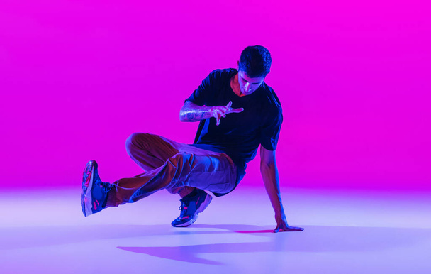 Portrait of dancing man, break dancer in action, motion in modern clothes isolated over bright magenta background at dance hall in neon light. - Fotografie, Obrázek