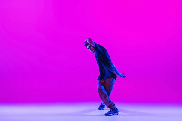 Portrait of dancing man, break dancer in action, motion in modern clothes isolated over bright magenta background at dance hall in neon light. - 写真・画像
