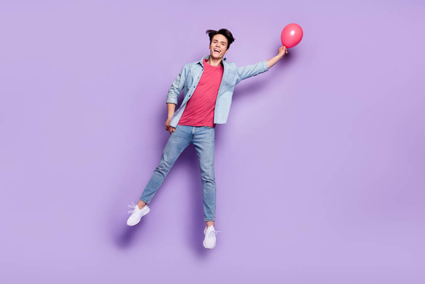 Full length photo of young guy happy positive smile birthday jump fly balloons isolated over purple color background - Foto, Imagen