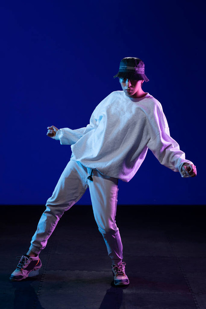 Latino boy dancing in studio with urban outfit and blue and purple background - Photo, Image