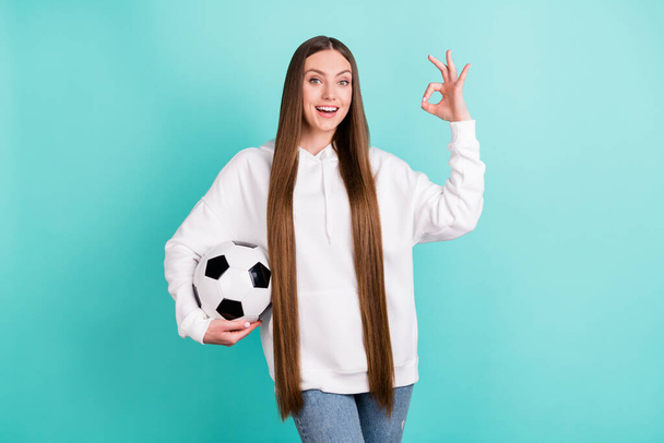 Portrait of attractive cheerful girl holding ball showing ok-sign isolated over bright teal turquoise color background - Zdjęcie, obraz