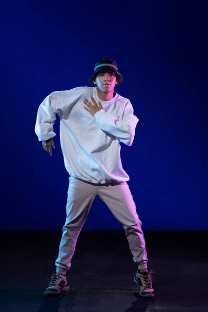 Latino-Junge tanzt im Studio mit urbanem Outfit und blauem und lila Hintergrund - Foto, Bild