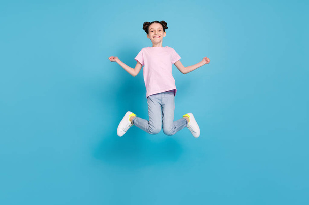 Photo of adorable sweet schoolgirl dressed pink t-shirt jumping high smiling isolated blue color background - Foto, Imagem