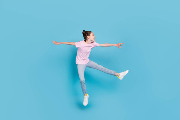 Photo of sweet funny schoolgirl dressed pink t-shirt jumping high looking empty space smiling isolated blue color background - Photo, Image