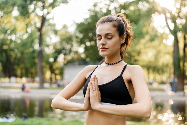 Mujer joven tranquila practica yoga y meditación mientras está de pie en el parque. Deportes al aire libre - Foto, imagen