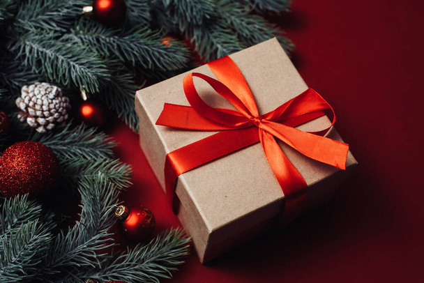 Concetto di sfondo natalizio. Confezione regalo di Natale con palla rossa e rami con pigne su sfondo rosso - Foto, immagini
