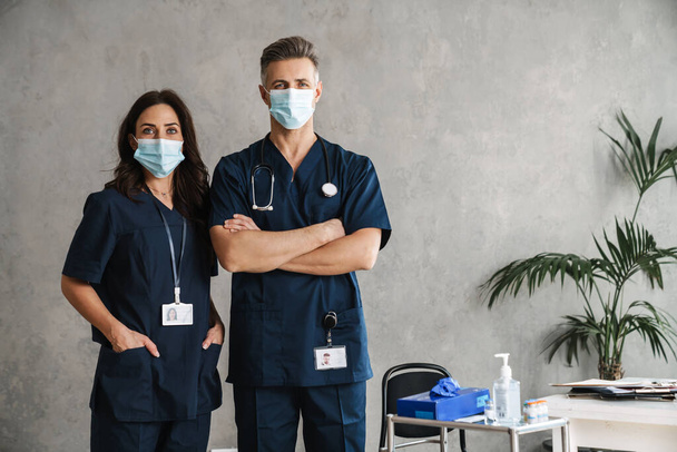 Two confident doctors in medical masks standing indoors - Foto, imagen