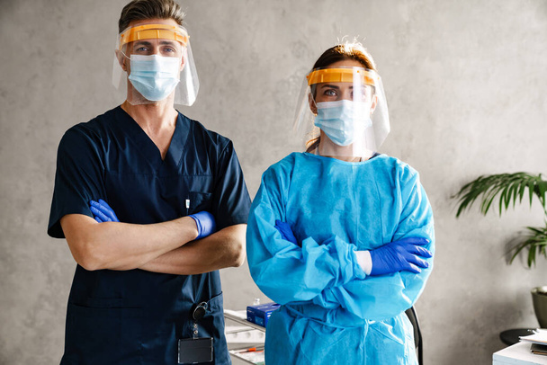 Two doctors wearing protective medical uniform standing in the cabinet, arms folded - Foto, Bild