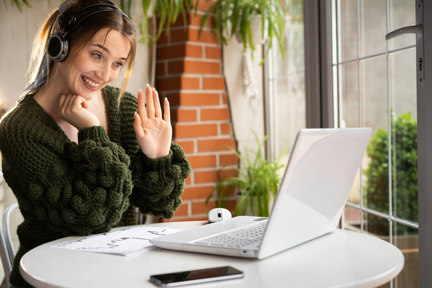 Счастливая белая женщина в беспроводной гарнитуре получает видеозвонок на ноутбук, используя веб-камеру, сидя в кафе. Чаттинг или удаленный учитель онлайн. Цифровое пользовательское и технологическое пространство - Фото, изображение