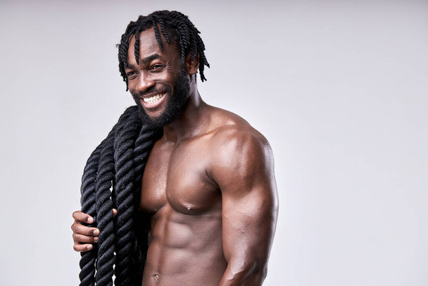Close-up portrait of positive smiling afro american guy holding battle ropes on shoulders - Foto, afbeelding