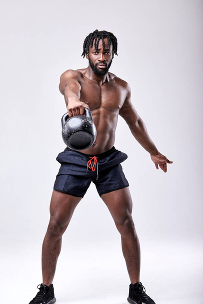Cross fit training. African sportsman doing weight training by lifting kettlebell - Foto, Imagen