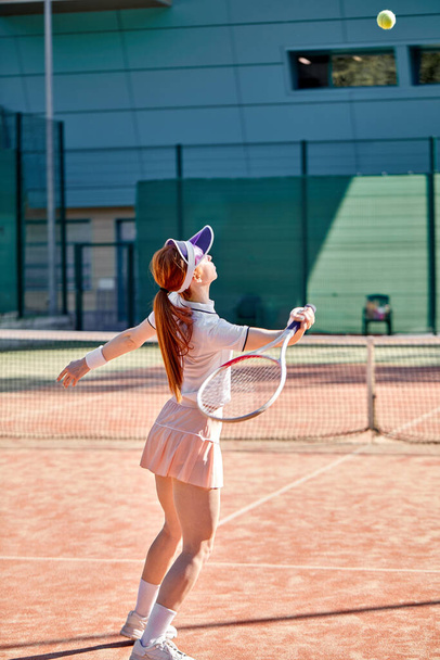 Young woman in white tennis uniform playing tennis, hits the ball with racket - Φωτογραφία, εικόνα