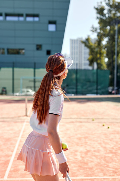 Rear view on pretty young woman in sexy sportwear playing tennis in city park - Zdjęcie, obraz
