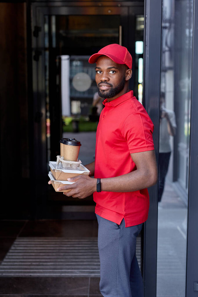 Delivery man holding takeaway food and drinks near house outdoors. Delivery service - Fotoğraf, Görsel