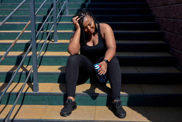 Exhausted Woman In Black Sportive Clothes Have Rest After Sport, Sitting With Water Bottle - Photo, Image