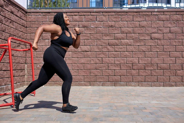 African woman jogging during cardio workout for burning calories outdoors in city - Photo, Image