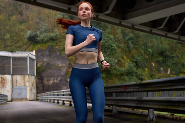 Portrait red-haired cute woman jogging on bridge alone in the morning, copy space - Fotó, kép