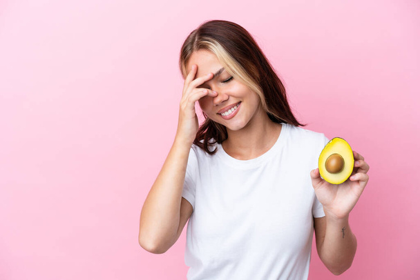 Young Russian woman holding avocado isolated on pink background laughing - Photo, Image