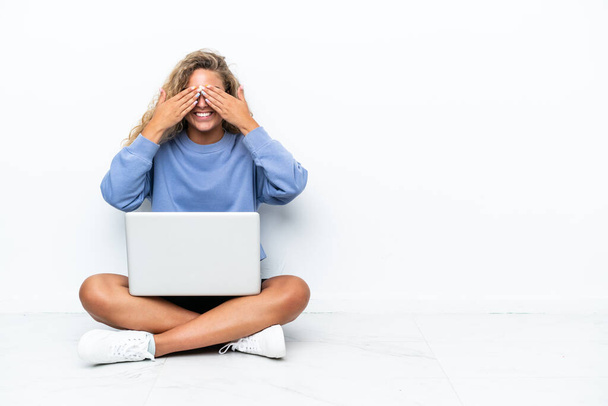 Chica con el pelo rizado con un ordenador portátil sentado en el suelo cubriendo los ojos por las manos - Foto, Imagen