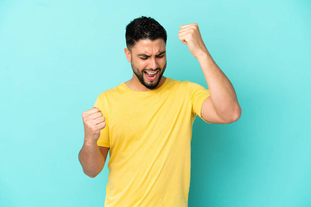 Young arab man isolated on blue background celebrating a victory - Photo, Image