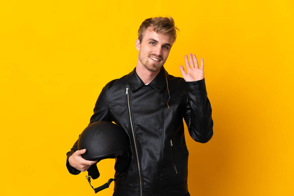 Man with a motorcycle helmet isolated on yellow background saluting with hand with happy expression - Фото, изображение