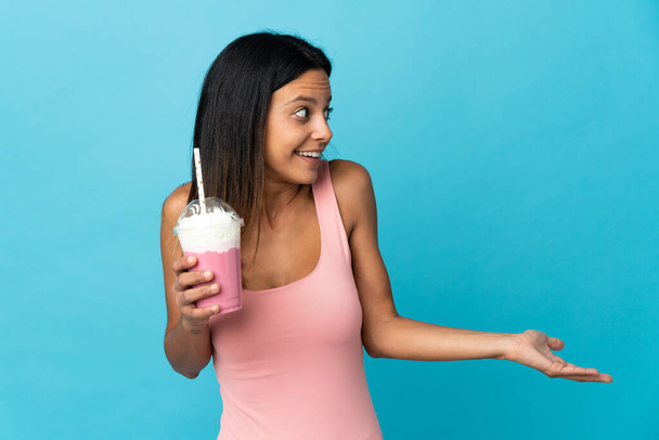 jonge vrouw met aardbei milkshake met verrassing uitdrukking terwijl op zoek kant - Foto, afbeelding