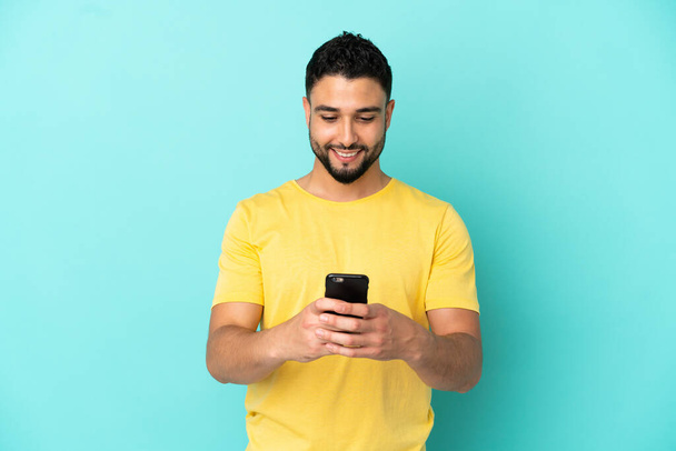 Fiatal arab férfi elszigetelt kék háttér küld egy üzenetet a mobil - Fotó, kép