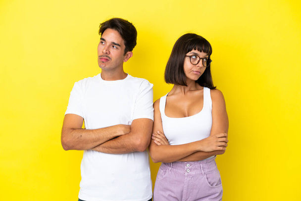 Young mixed race couple isolated on yellow background with confuse face expression while bites lip - Photo, Image