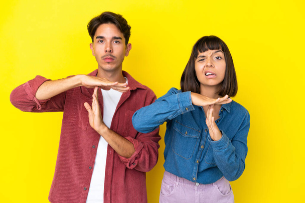 Молодая пара смешанной расы изолированы на желтом фоне делает остановку жест рукой, чтобы остановить действие - Фото, изображение