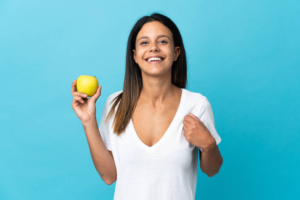 Caucasian girl isolated on blue background with an apple and happy - Φωτογραφία, εικόνα
