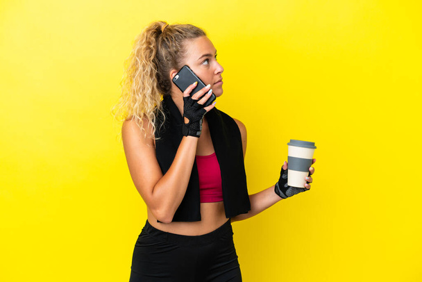 Donna sportiva con asciugamano isolato su sfondo giallo contenente caffè da portare via e un cellulare - Foto, immagini