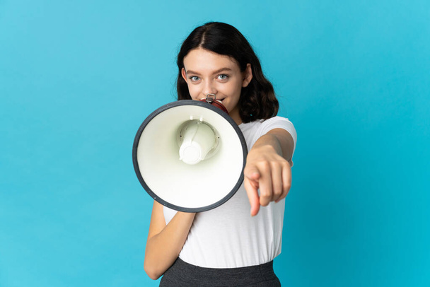 Teenager Ukrainian girl isolated on white background shouting through a megaphone to announce something while pointing to the front - 写真・画像
