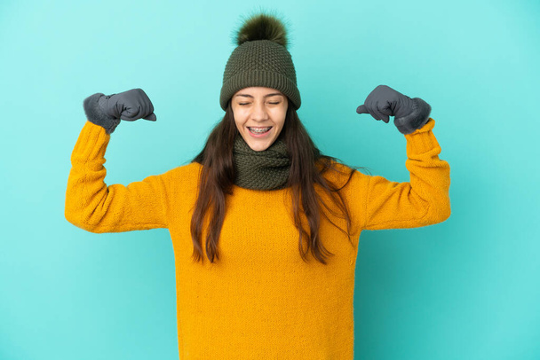 Young French girl isolated on blue background with winter hat doing strong gesture - Photo, Image