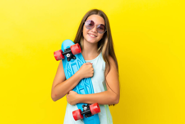 Kleine kaukasische Skater Mädchen isoliert auf gelbem Hintergrund mit einem Schlittschuh mit glücklichem Ausdruck - Foto, Bild