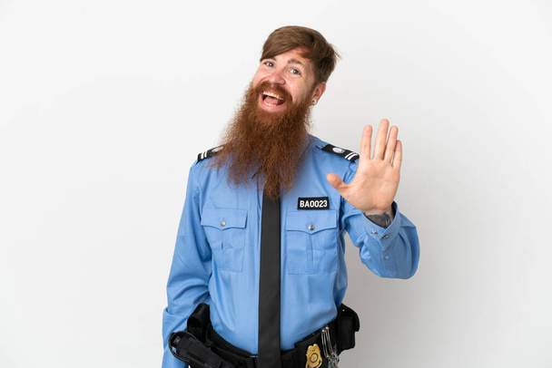 Rotschopf Polizist isoliert auf weißem Hintergrund salutiert mit fröhlichem Gesichtsausdruck mit der Hand - Foto, Bild
