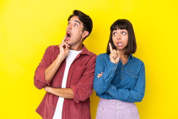 Young mixed race couple isolated on yellow background thinking an idea pointing the finger up - Photo, Image